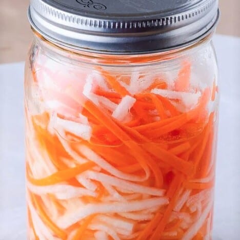 A canning jar filled with julienned carrots and daikon radish.