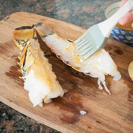 Lobster tail halves having a seasoned butter brushed on them.