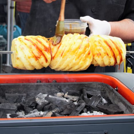 The maple bourbon glaze being applied to three pineapples over a spit.