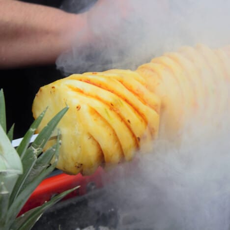 Fresh pineapple on a spit with smoked surounding it.