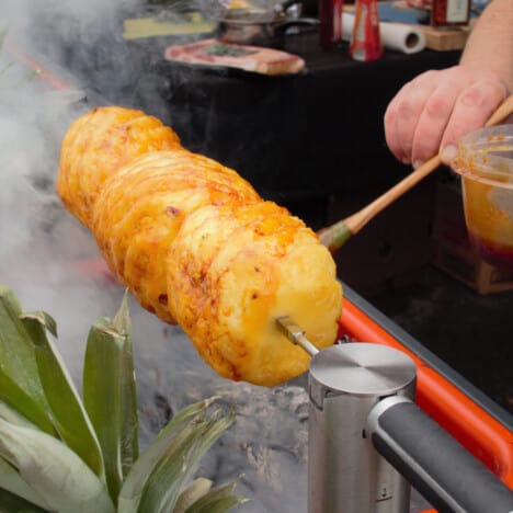 Three whole pineapples on a spit being basted in the glaze.