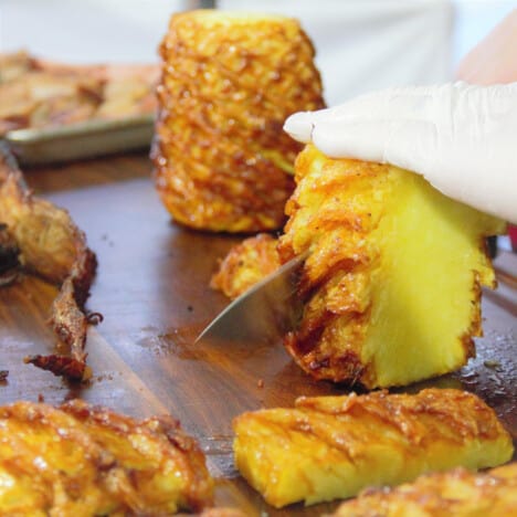 A cooked whole pineapple being cut into serving sized pieces.