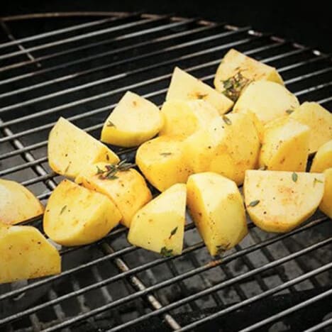 Pieces of potato covered in a herb oil cooking on a grill.