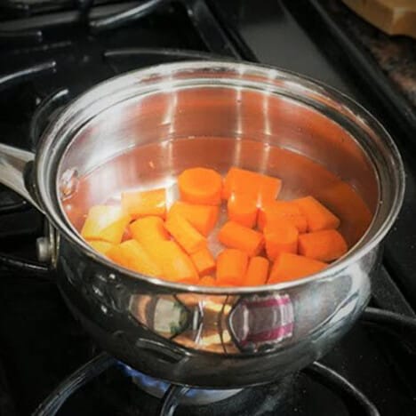 Cut carrots in a saucepan of water on a gas stove.