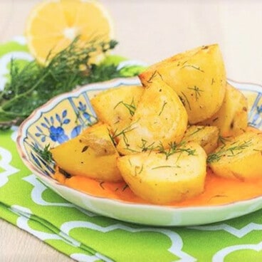 Baked potatoes served in a shallow bowl in a carrot sauce and garnished with dill.
