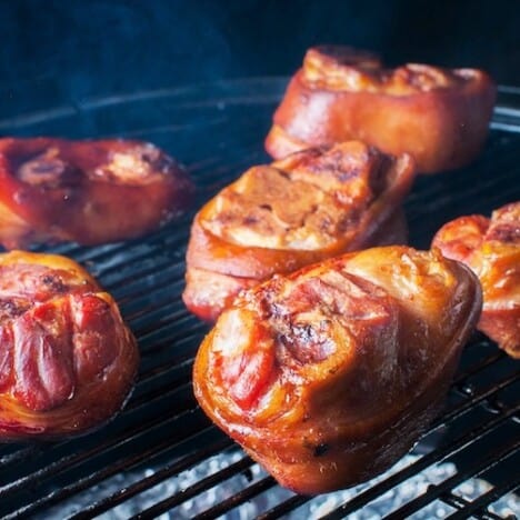 Ham hocks, smoked to a dark red, are sitting on a grill grate.