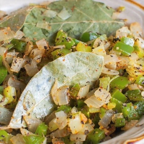 A close up shot of cooked onions, green bell peppers, celery, and bay leaves.