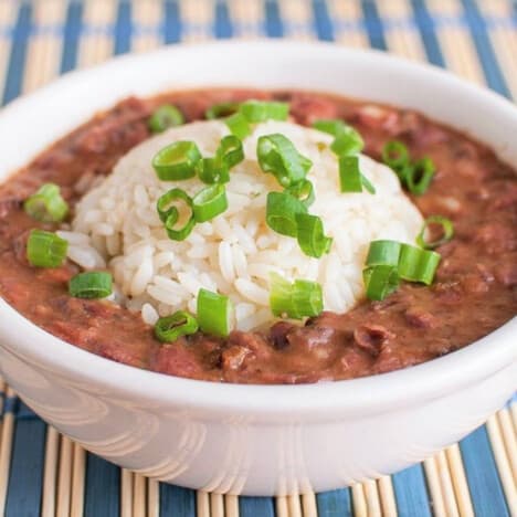 A bowl of cooked red bean stew topped with a scoop of white rice and sliced green onions on a blue and white stripped placemat.