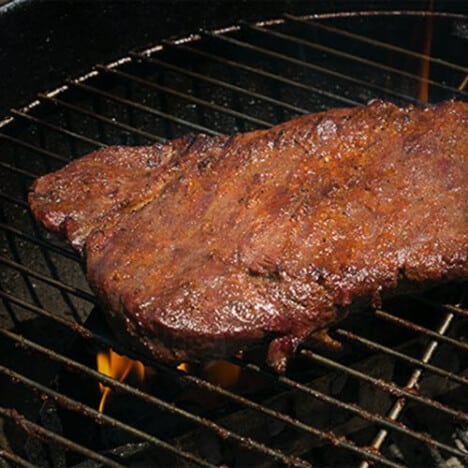 A seasoned flat iron steak is cooking a grill grate.