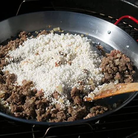 Paella dish with cooked ground sausage topped with raw rice.