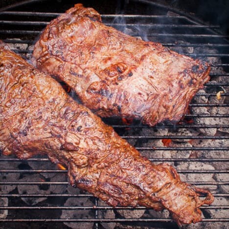 Two pieces of skirt steak grilling over charcoal.