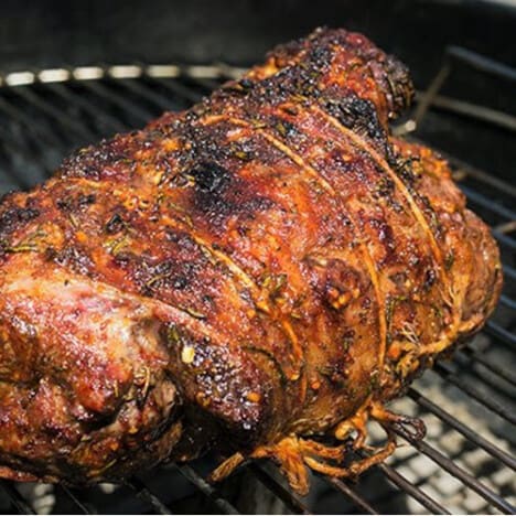 A charred, smoked roll of lamb sits on a grill grate.