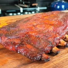 Full rack of cooked ribs resting on a wooden chopping board.