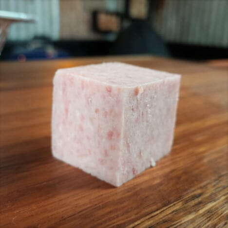 A perfect cube of spam on a wooden chopping board.