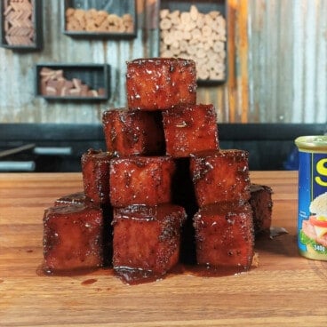 A block tower of burnt end spam cubes on a wooden chopping board.