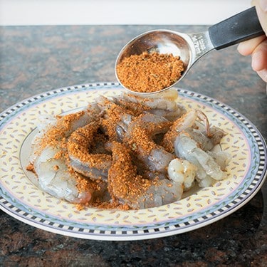 A plate of raw shrimp being seasoned with rub.