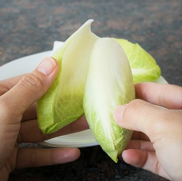 A pair of white hands peeling apart Belgian endive leaves.