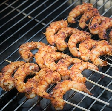 Seasoned shrimp are skewered on two skewers on the grill.