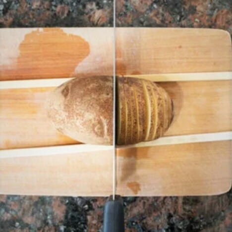 A baking potato being sliced part way through with two wooden spoon handles either side.