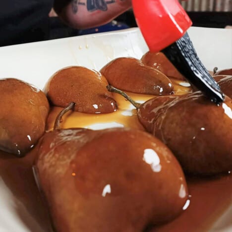 Basting brush coating halved pears in a white baking tray with a glaze.