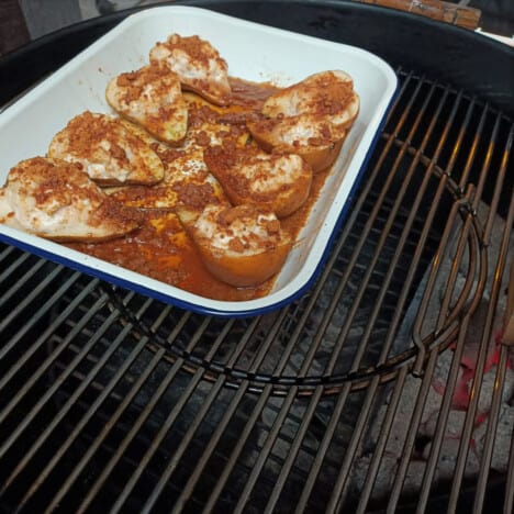 A whitehite baking tray filled with stuffed pears sitting in a kettle grill set up for indirect cooking.