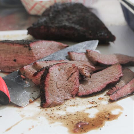 Smoked tri-tip being thinly sliced against the grain.