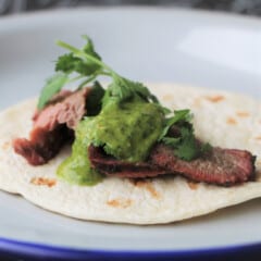 A plate with a tortilla topped with tri-tip and pineapple chimichurri sauce, garnished with fresh cilantro.