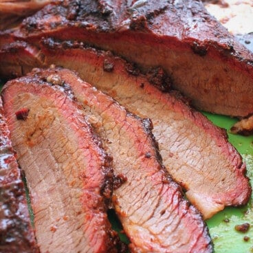 Slices of juicy brisket with a rich crust on a green cutting board.
