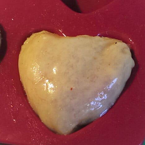 A single heart-shaped chicken thigh with skin-on in a red silicone mold.