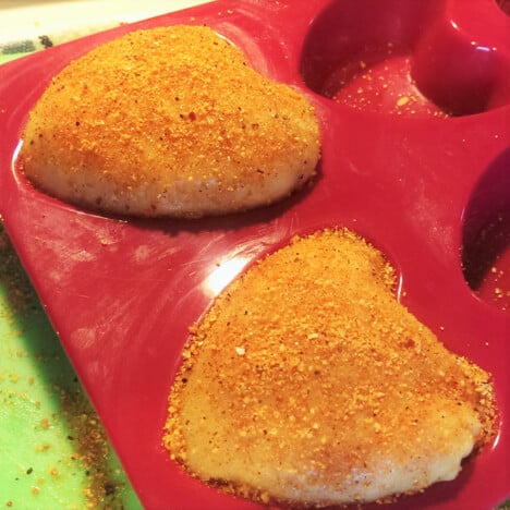 Looking down on two seasoned raw chicken thighs formed into heart-shaped molds.