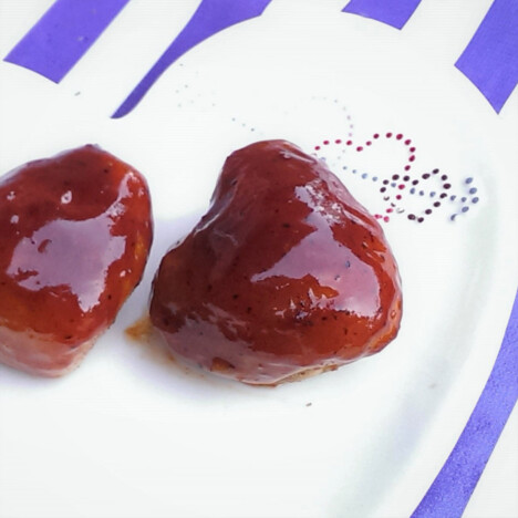 Two glazed heart-shaped chicken thighs on a white plate with a blue stripped background.