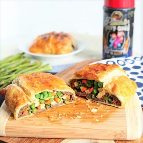 A vegetable wellington served on a wooden chopping board sliced in half exposing the filling in side.