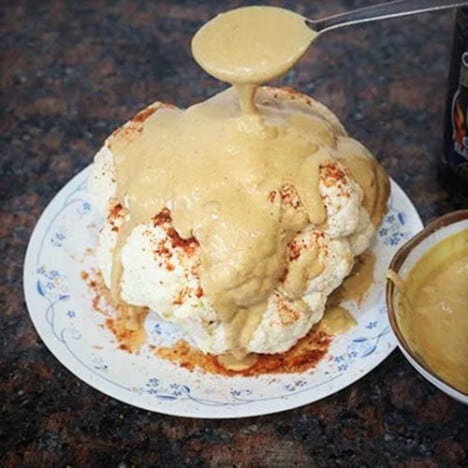 Curry sauce being spooned over a whole cauliflower.