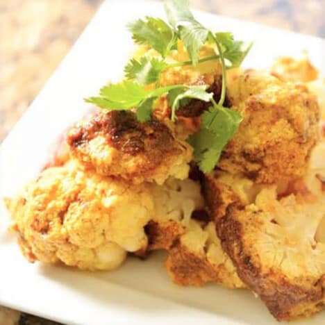 Curried cauliflower served on a square white plate.