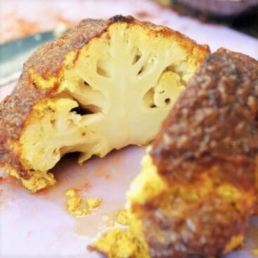A cooked curried cauliflower sliced in half exposing the orange tinted insides.