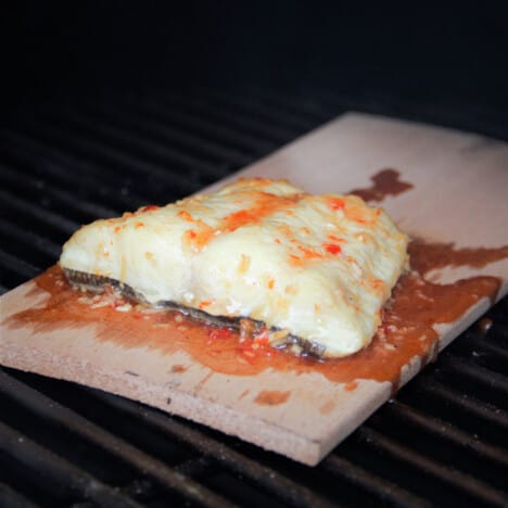 Grilling plank in a barbecue with sweet chili fish fillet on it.