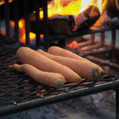 Four large carrots cooking on a live fire grill.