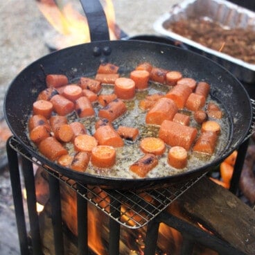 A gentle fire with a skillet of chunky carrots cooking above it.