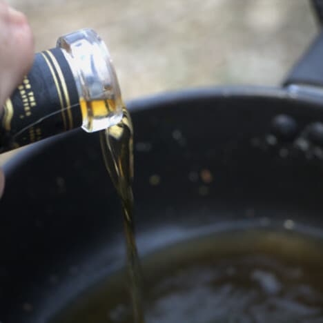 A bottle pouring a gentle stream of bourbon into a saucepan.