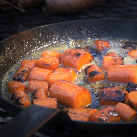 Close look of a skillet filled with large chunks of carrots in a bubbling bourbon sauce.