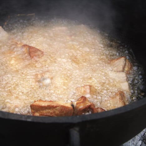 A Dutch oven with oil bubbling heavily with a few pieces of chicharron visible.