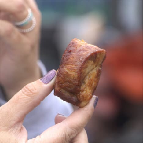 A Chicharron being held between two fingers with purple nail polish.
