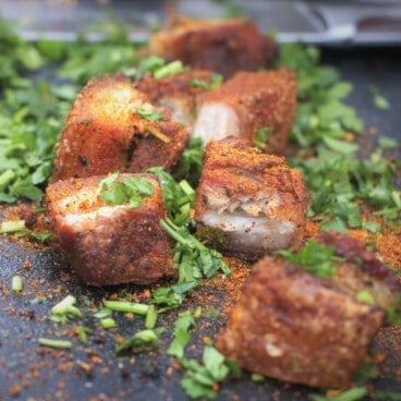 Black serving tray with chicharron garnished with a BBQ rub and cut cilantro.