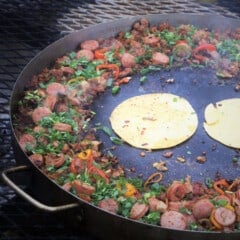 A discada with the edges filled with a colorful meat and bell pepper filling while frying corn tortillas in the center.