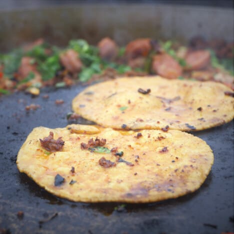 Two corn tortillas cooking in the discada with the filling ingredients in the background.