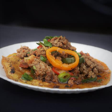 A corn tortilla is topped with a meat mixture and garnished with a slice yellow bell pepper.